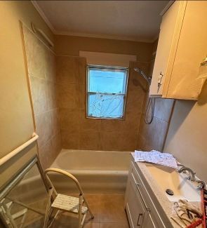 A bathroom with a tub , sink , mirror and window.