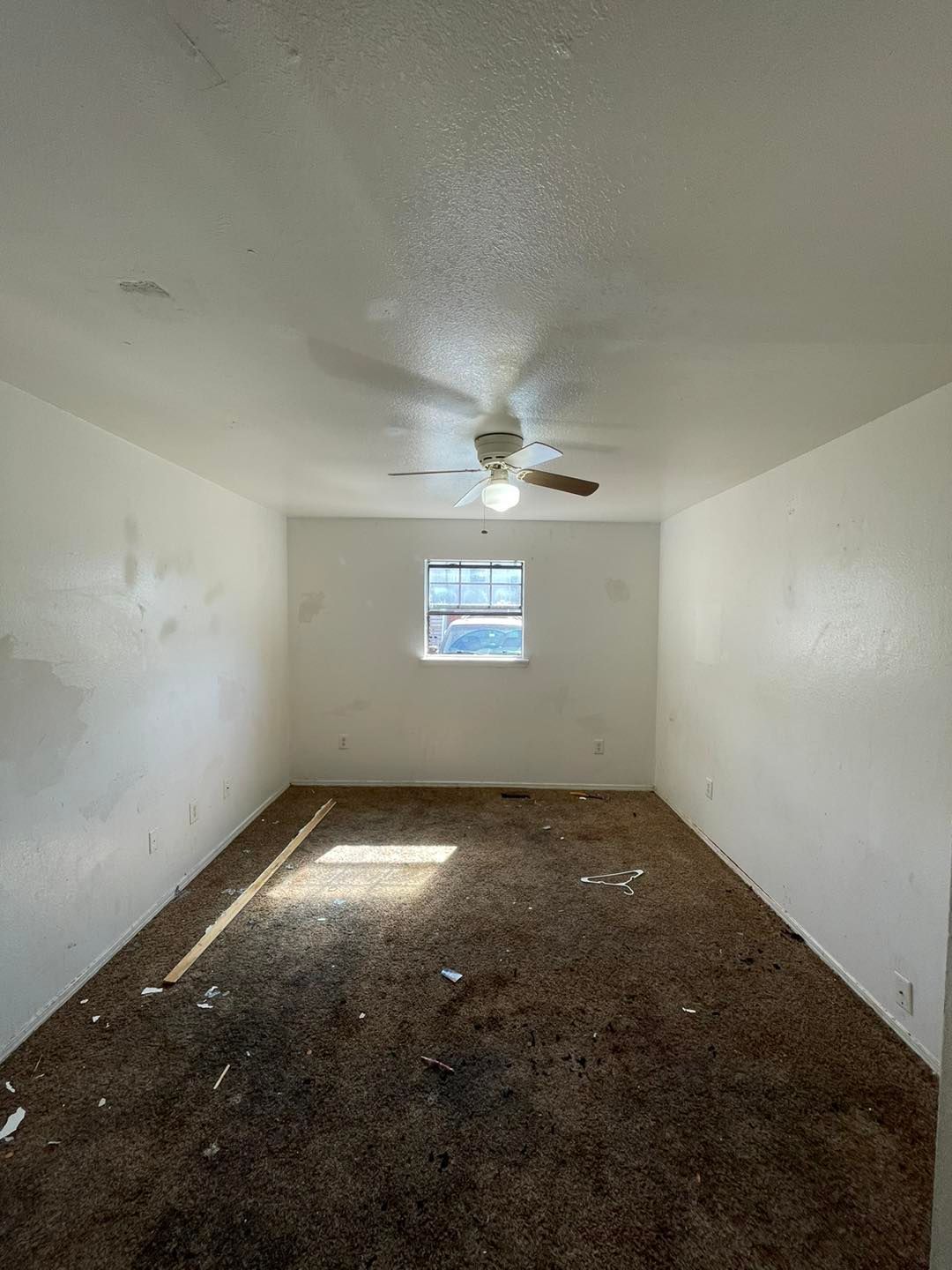 An empty room with a ceiling fan and a window.