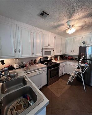 A kitchen with white cabinets , stainless steel appliances , a sink , and a ladder.