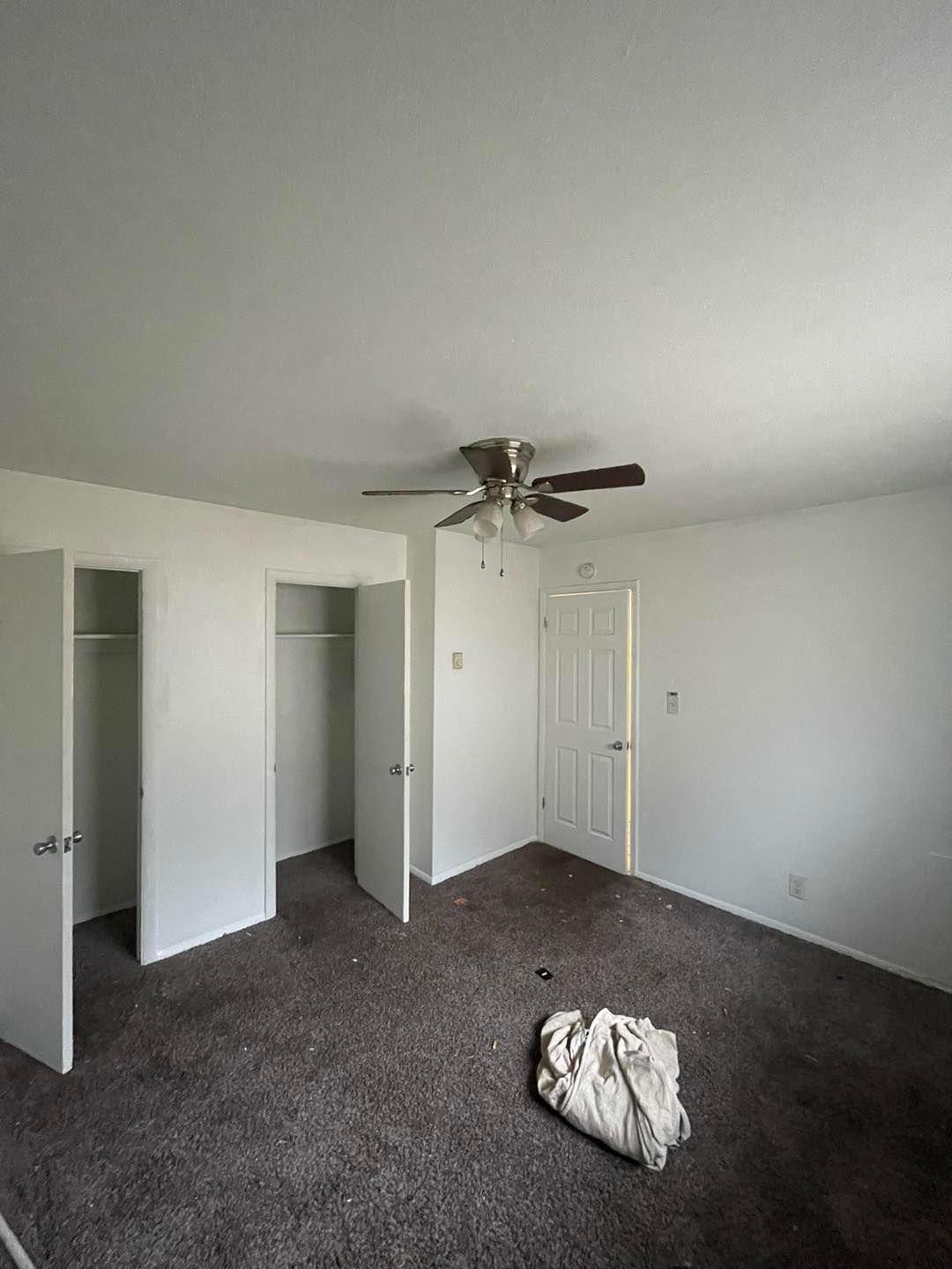 An empty bedroom with a ceiling fan and closets.