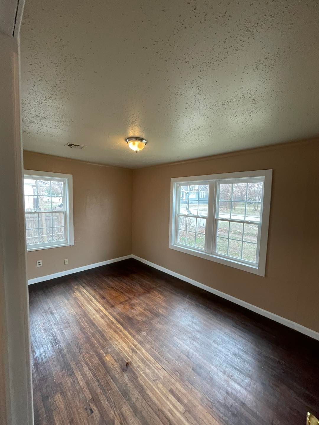 An empty living room with hardwood floors and two windows.