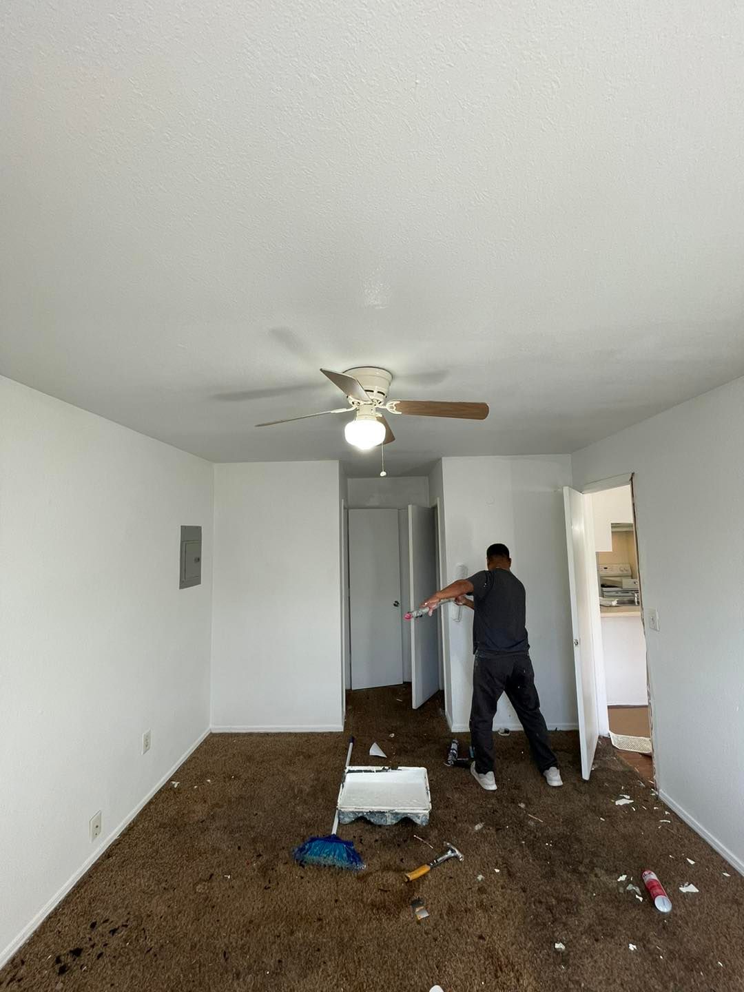 A man is standing in an empty room with a ceiling fan.