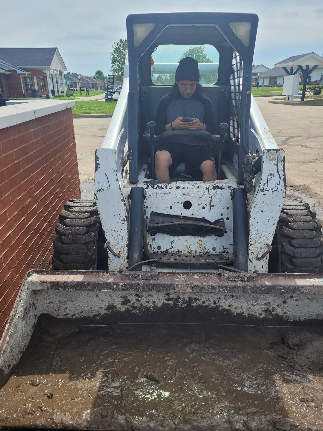 A man is sitting on a bulldozer looking at his phone.