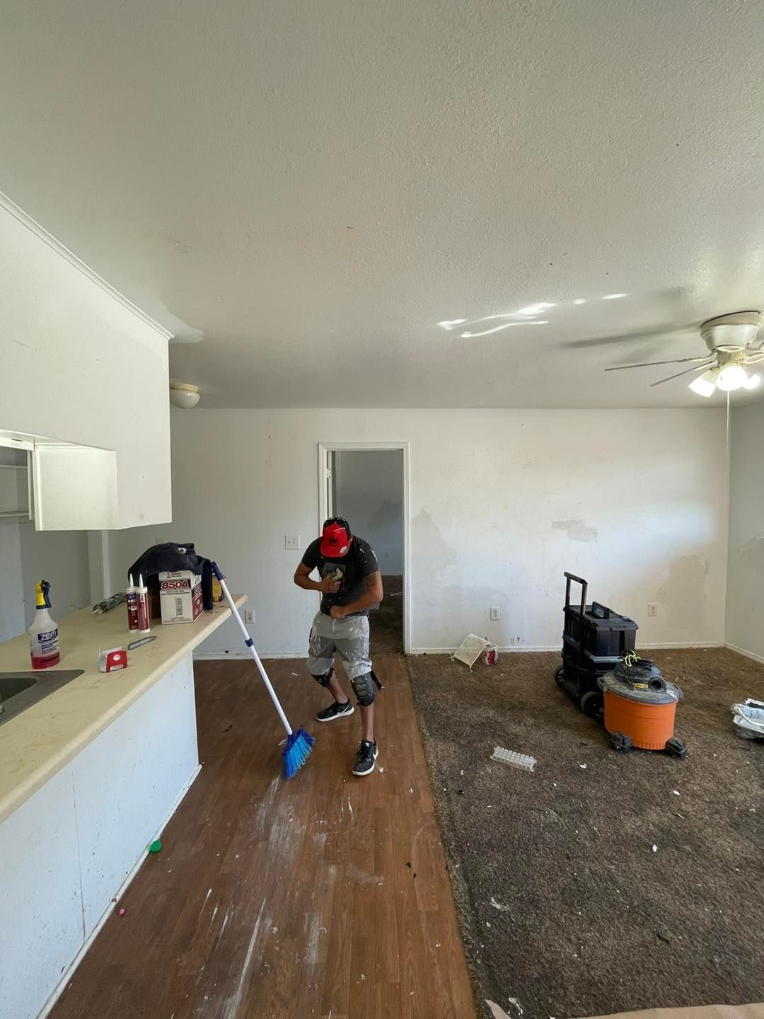 A man is cleaning the floor of a living room with a broom.