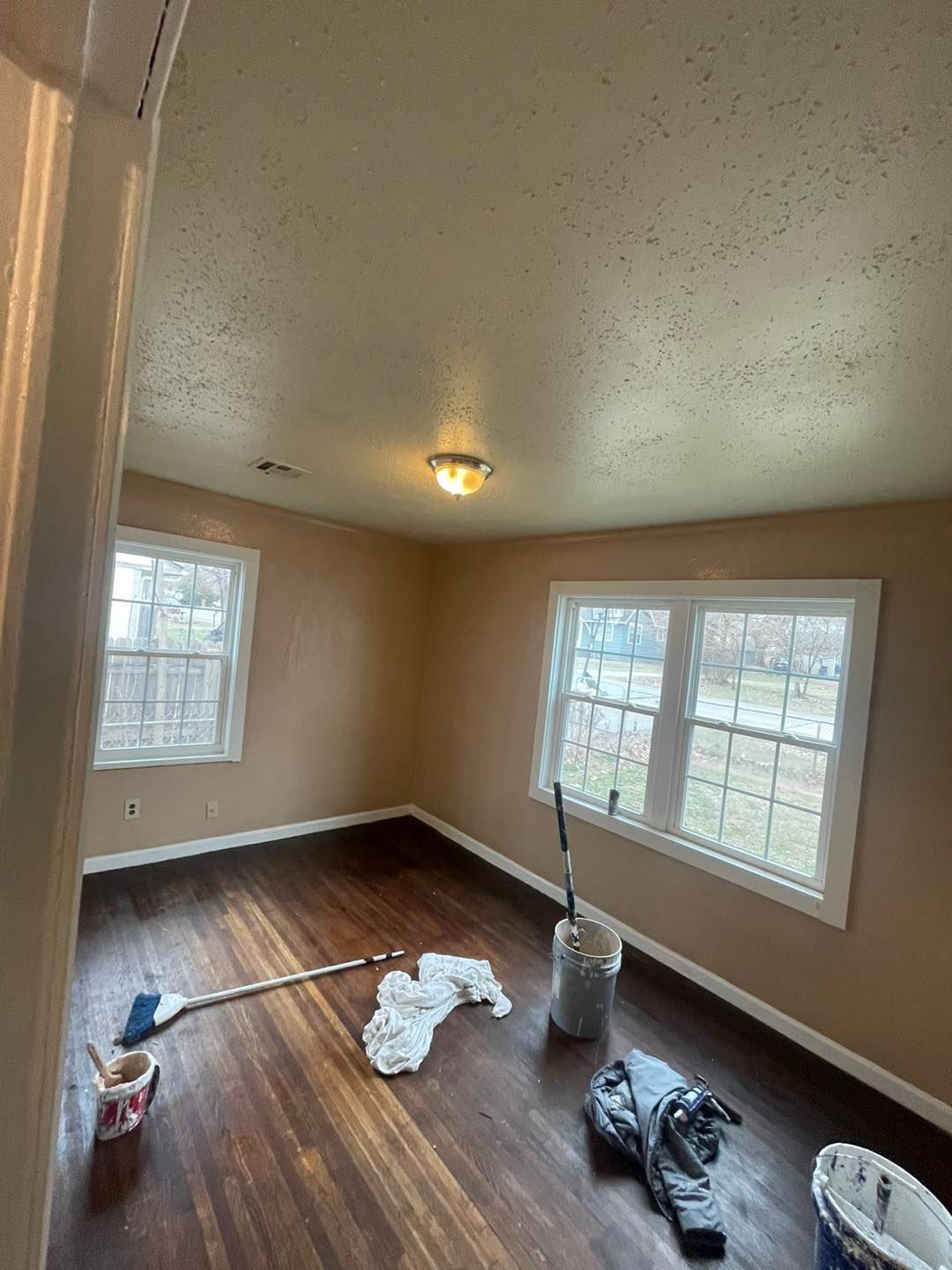 A room with hardwood floors and two windows is being painted.