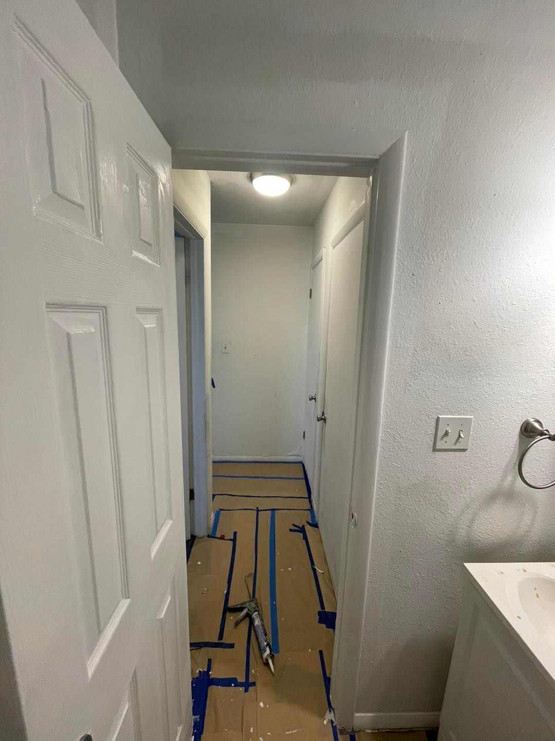 A hallway with a white door and blue tape on the floor.