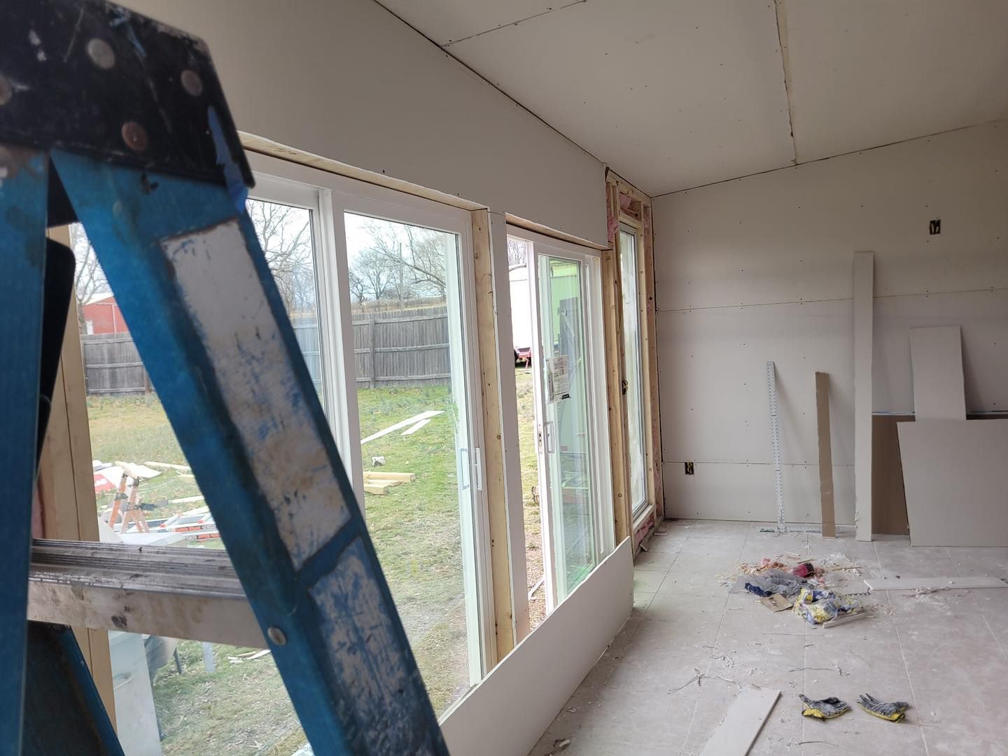 A blue ladder is sitting in a room with a lot of windows.