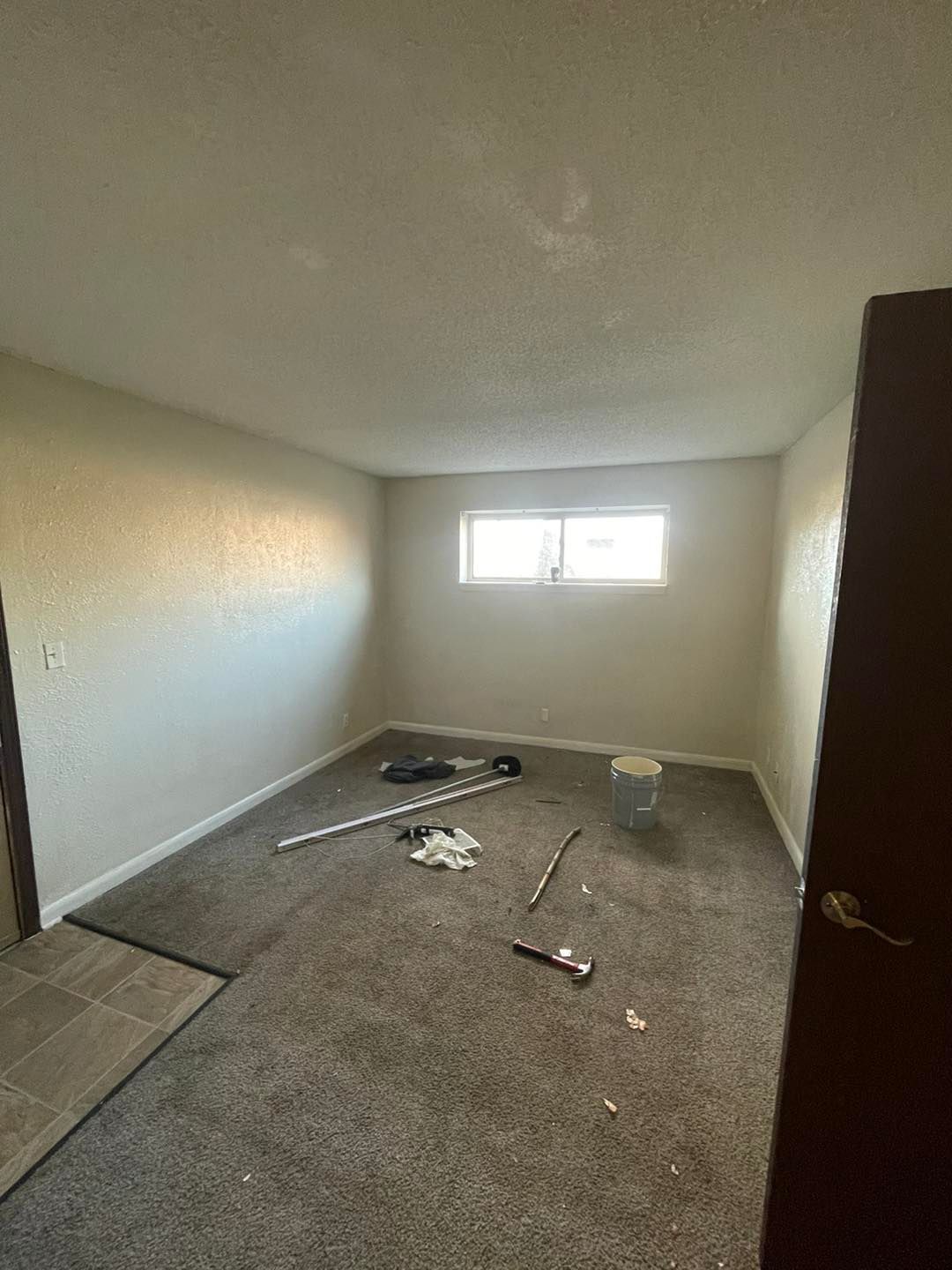 An empty room with a window and a bucket on the floor.