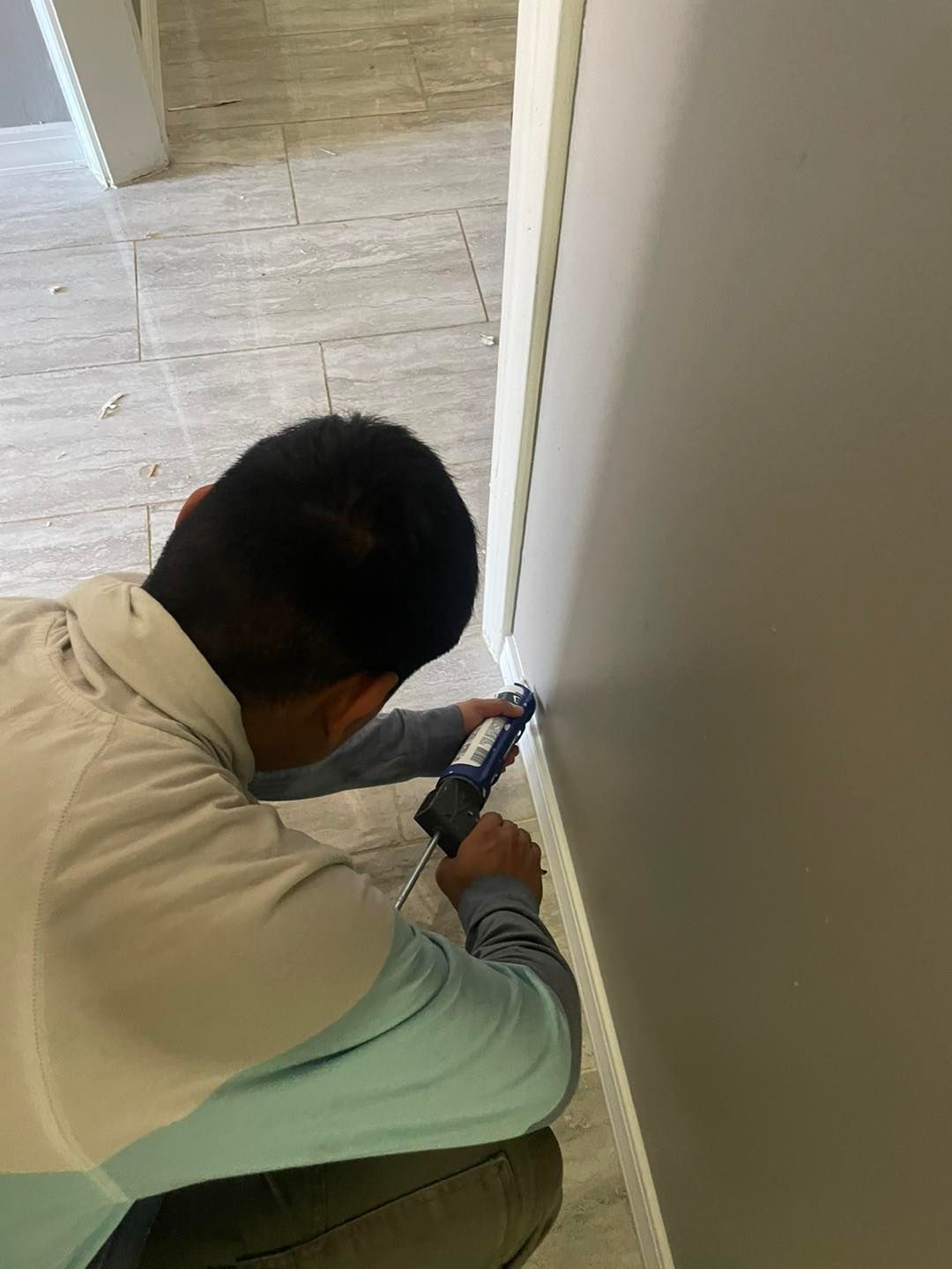 A man is kneeling down and using a tool on a wall.