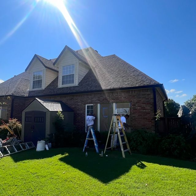 A man is standing on a ladder in front of a brick house.