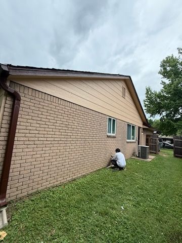 A man is kneeling in the grass in front of a brick house.