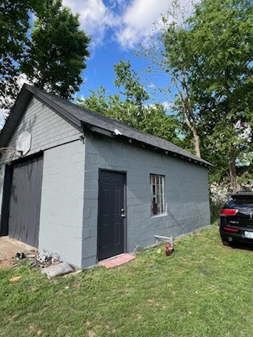 A car is parked in front of a gray garage.
