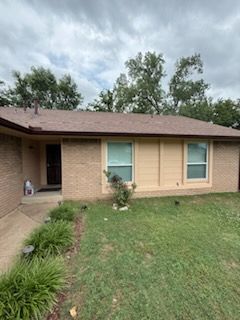 A brick house with a brown roof and a large lawn in front of it.
