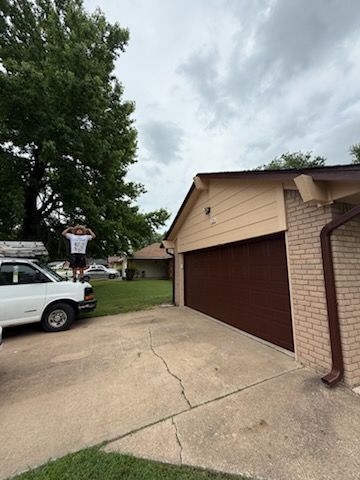 A man is standing in front of a garage door in a driveway.