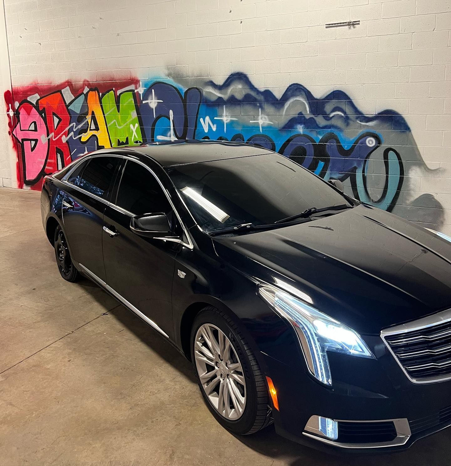 A black car is parked in front of a wall with graffiti on it