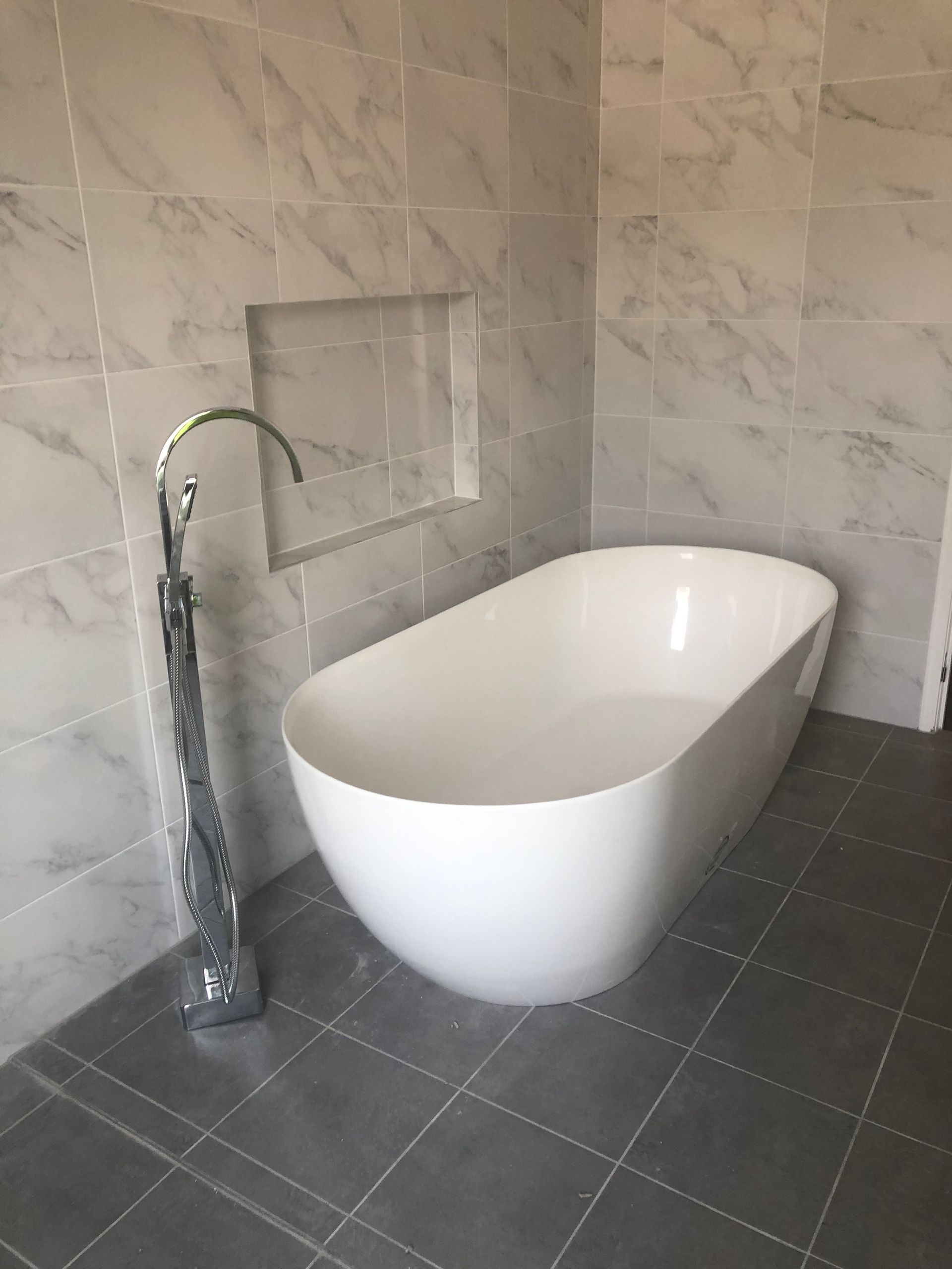 A white bathtub is sitting on a tiled floor in a bathroom.