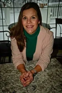 tracy hess intuitive eating counsel sitting at a table with her hands folded and smiling.