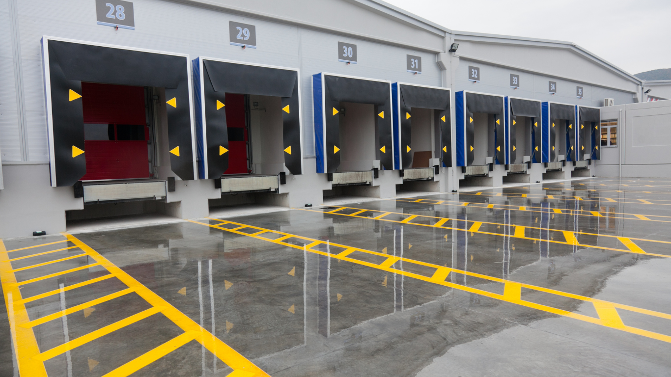Loading docks of a warehouse, with open bays and yellow markings on wet concrete.
