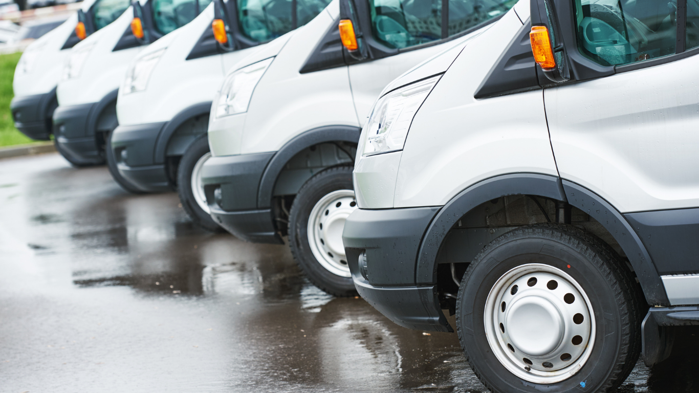 Line of silver vans parked on wet asphalt.