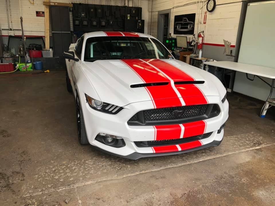 A white mustang with red stripes is parked in a garage