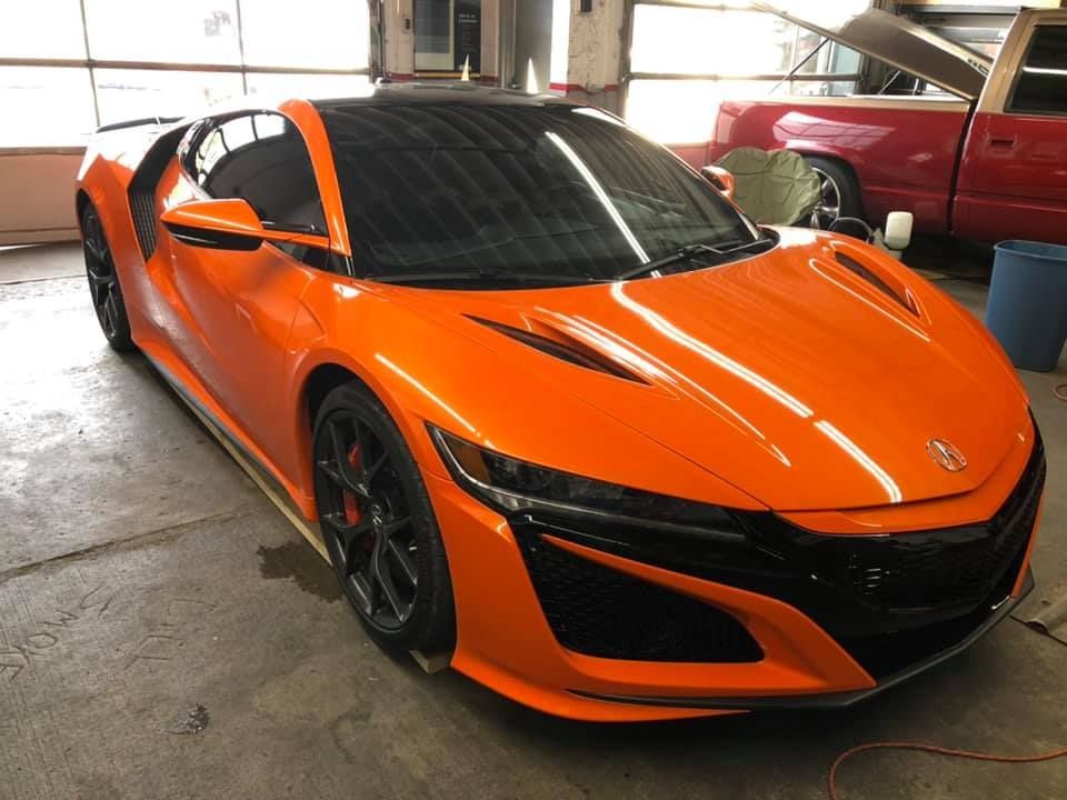 An orange sports car is parked in a garage next to a red truck