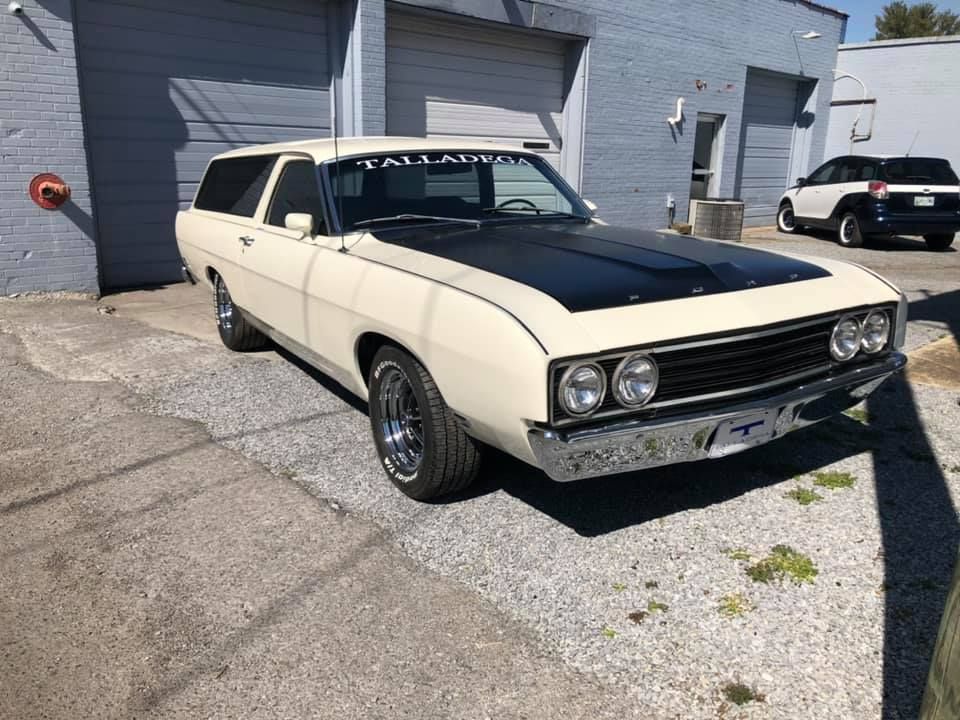 A white car with a black hood is parked in front of a building.