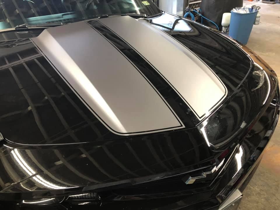 A black car with silver stripes on the hood is parked in a garage.