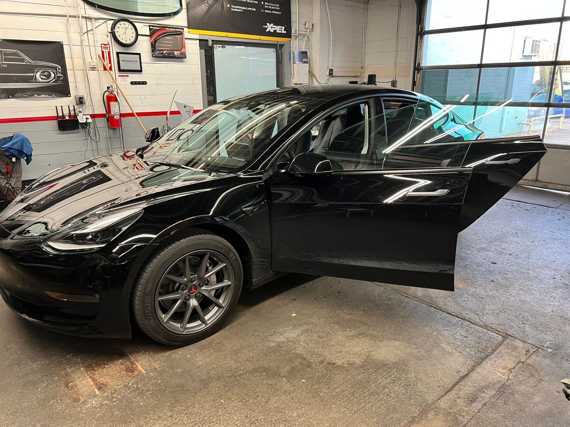 A black tesla model 3 is parked in a garage with its doors open.