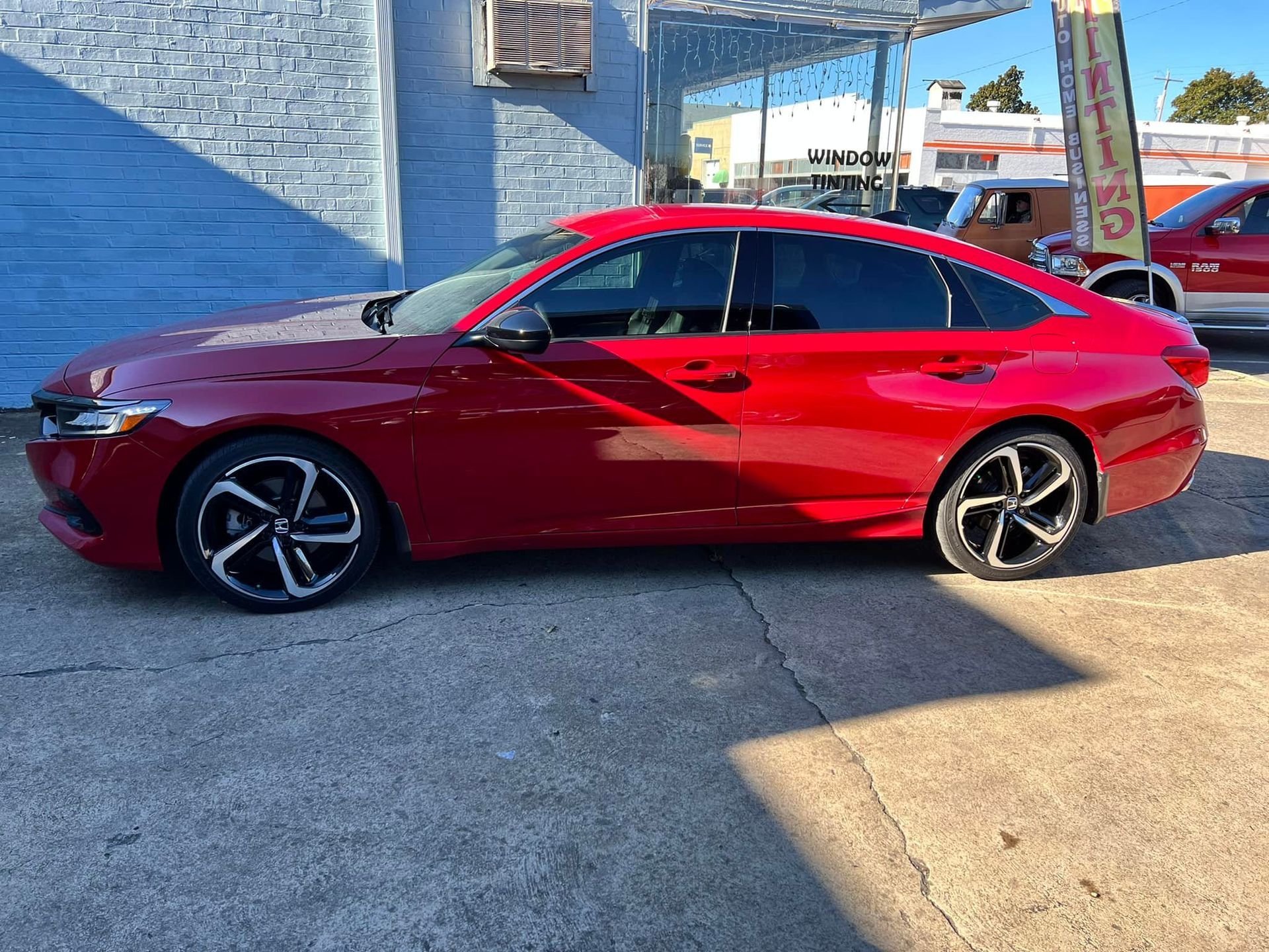 A red car is parked in a parking lot in front of a building.