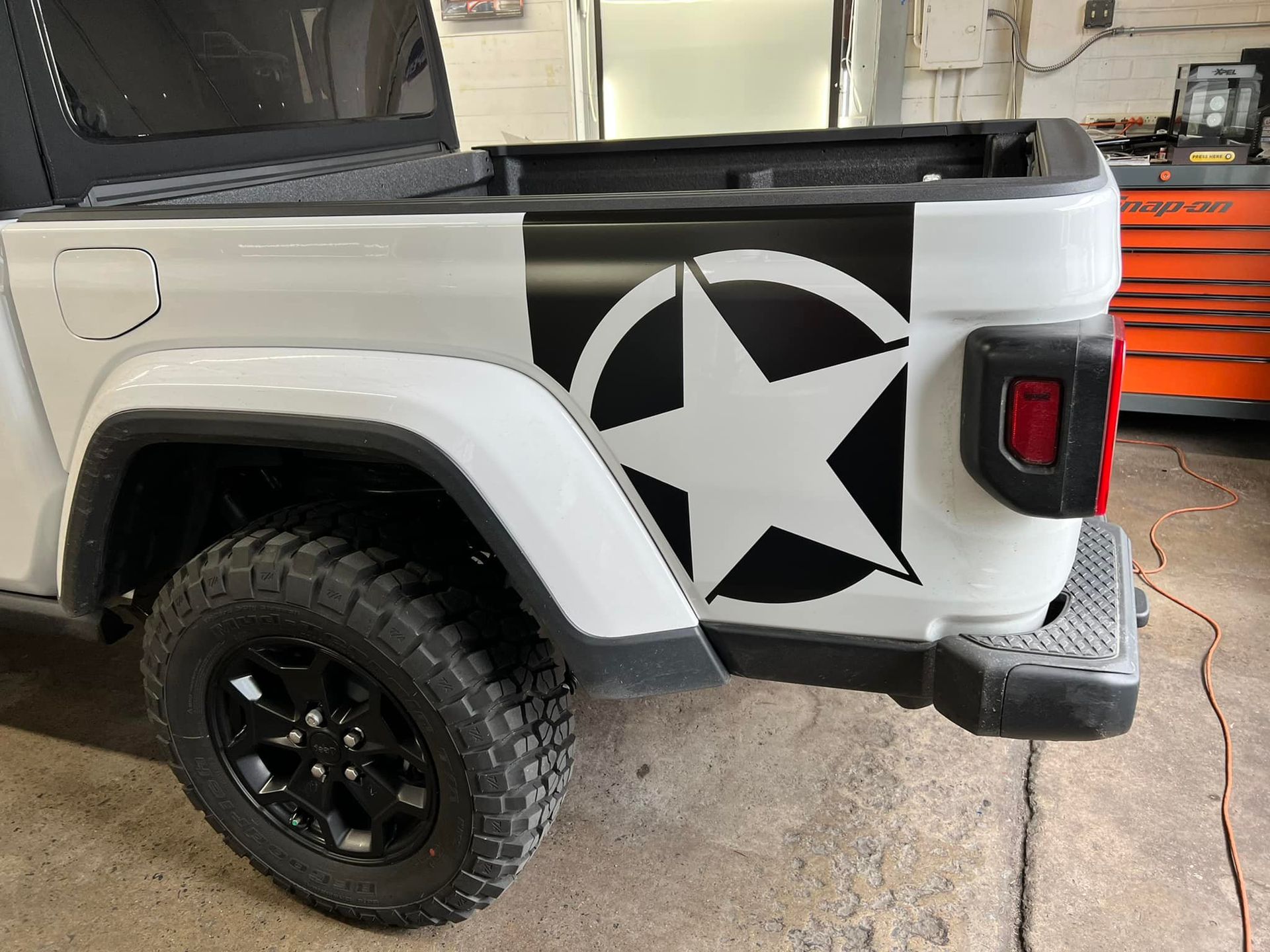 A white jeep with a black star on the side is parked in a garage.