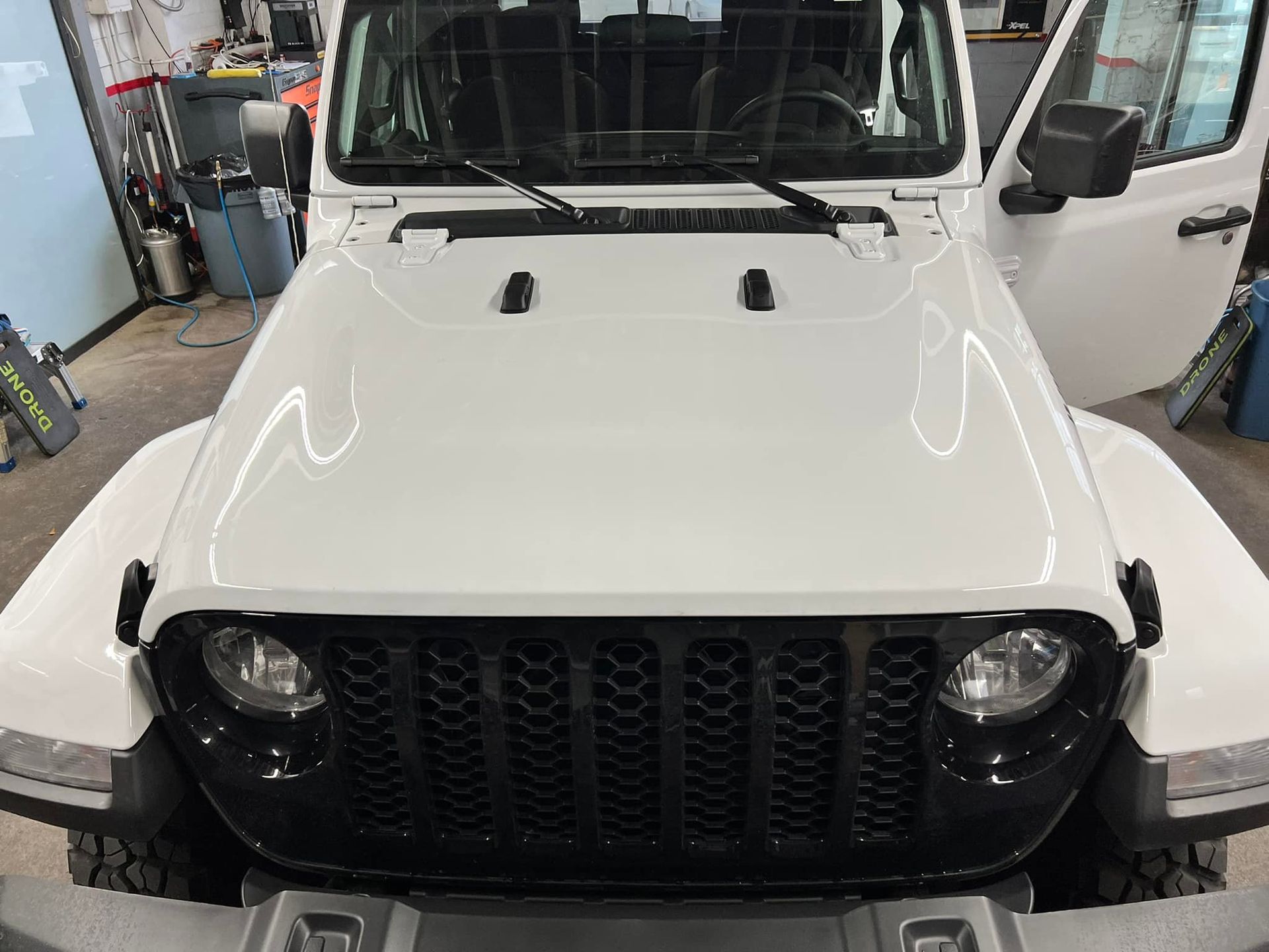 A white jeep with a black grille is parked in a garage.