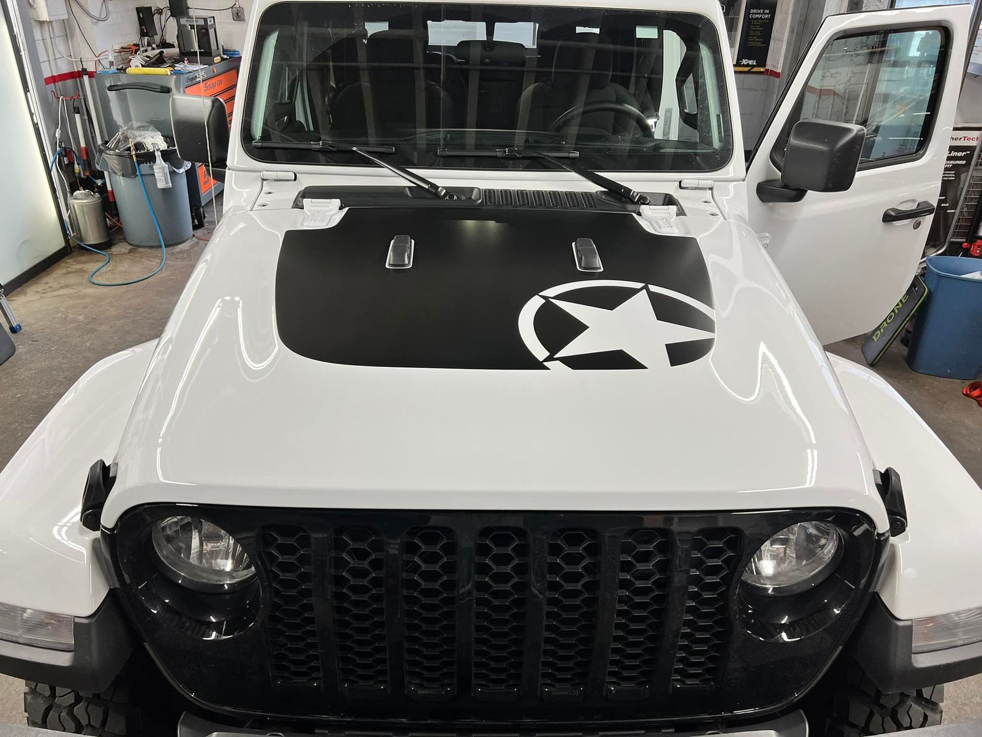 A white jeep with a black star on the hood is parked in a garage.