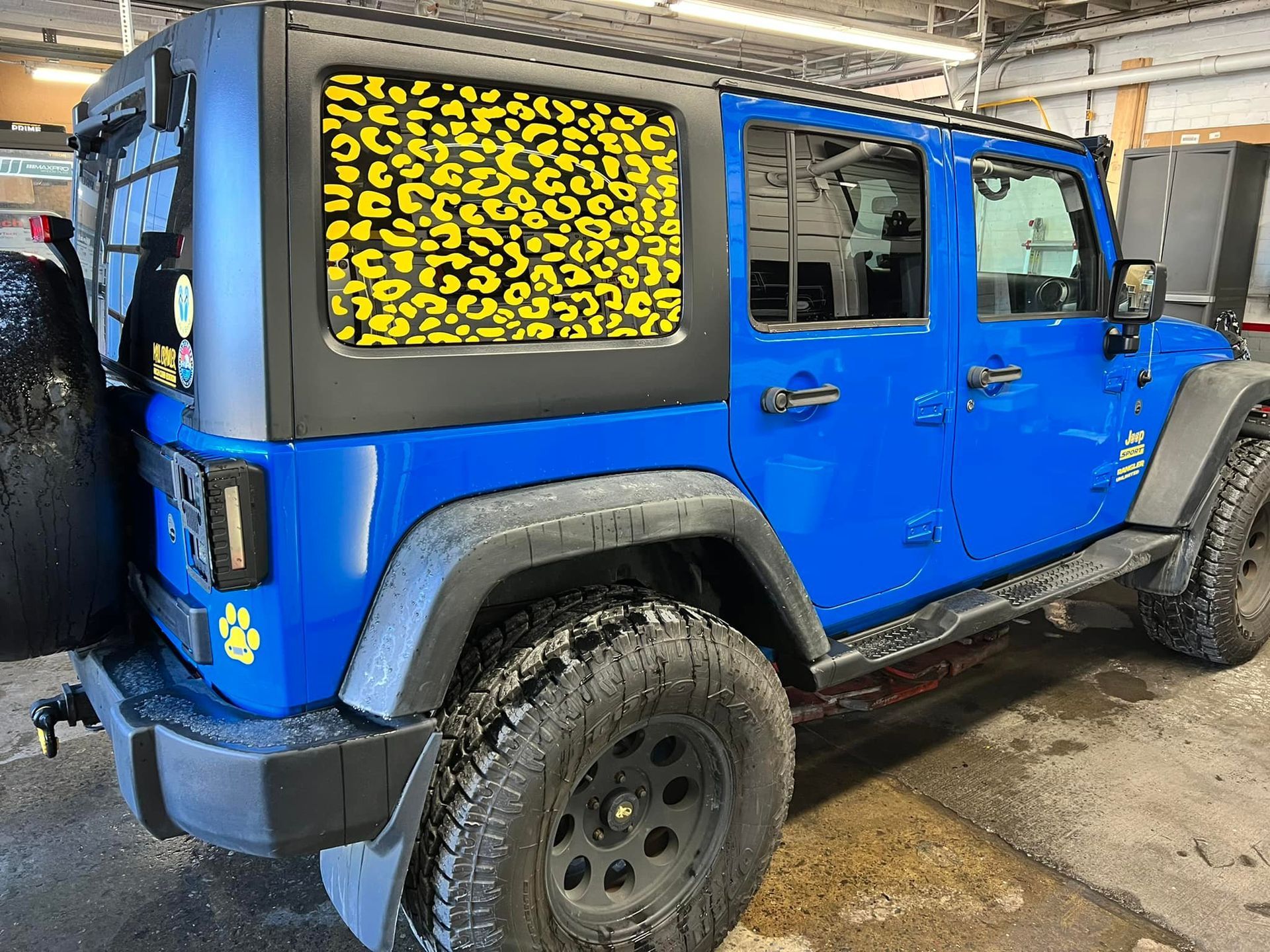 A blue jeep with yellow leopard print windows is parked in a garage.