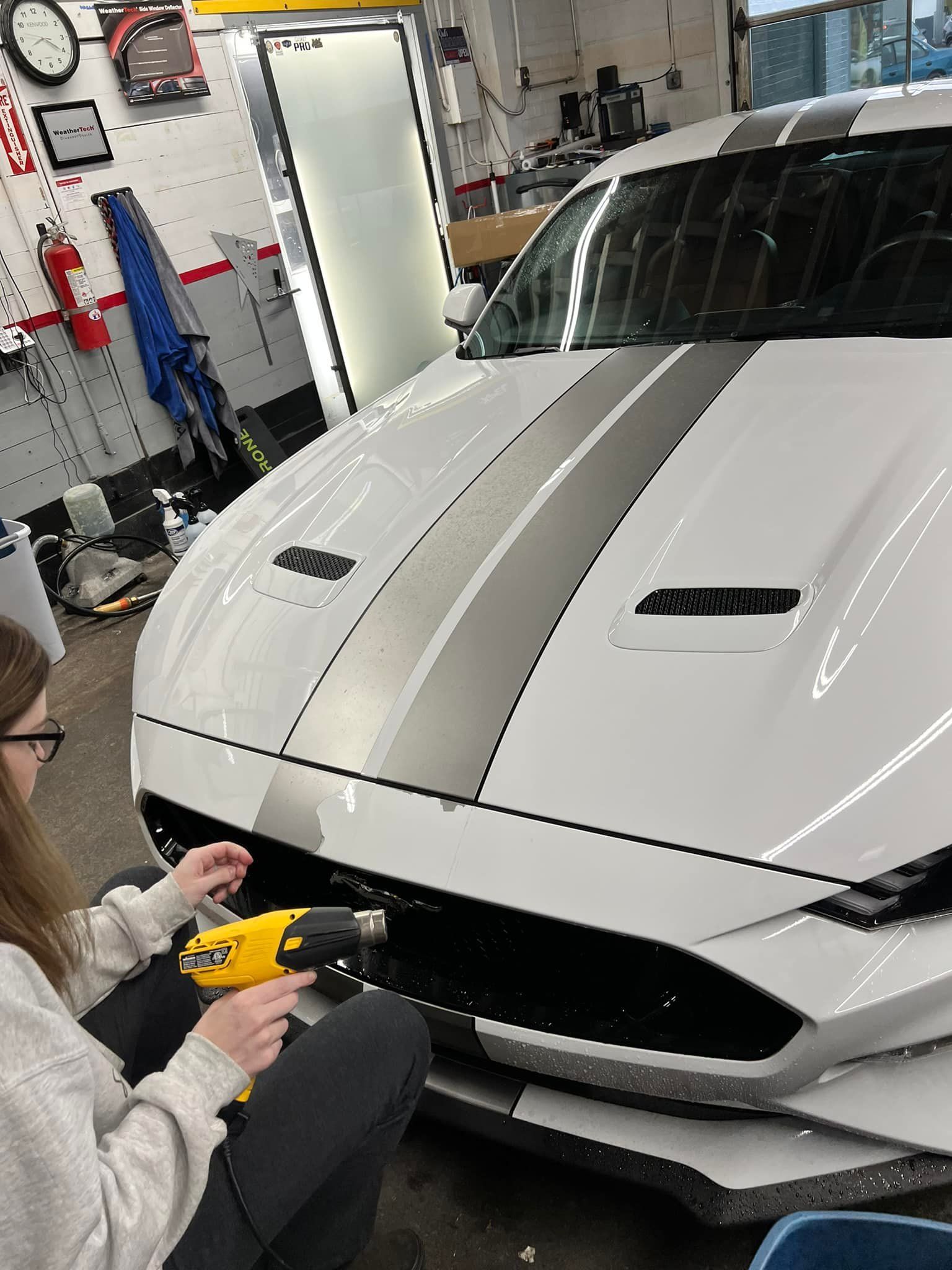 A woman is working on a white car in a garage.
