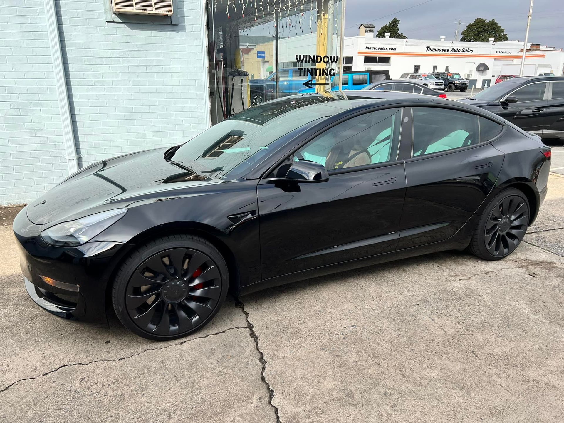 A black tesla model 3 is parked in front of a building.