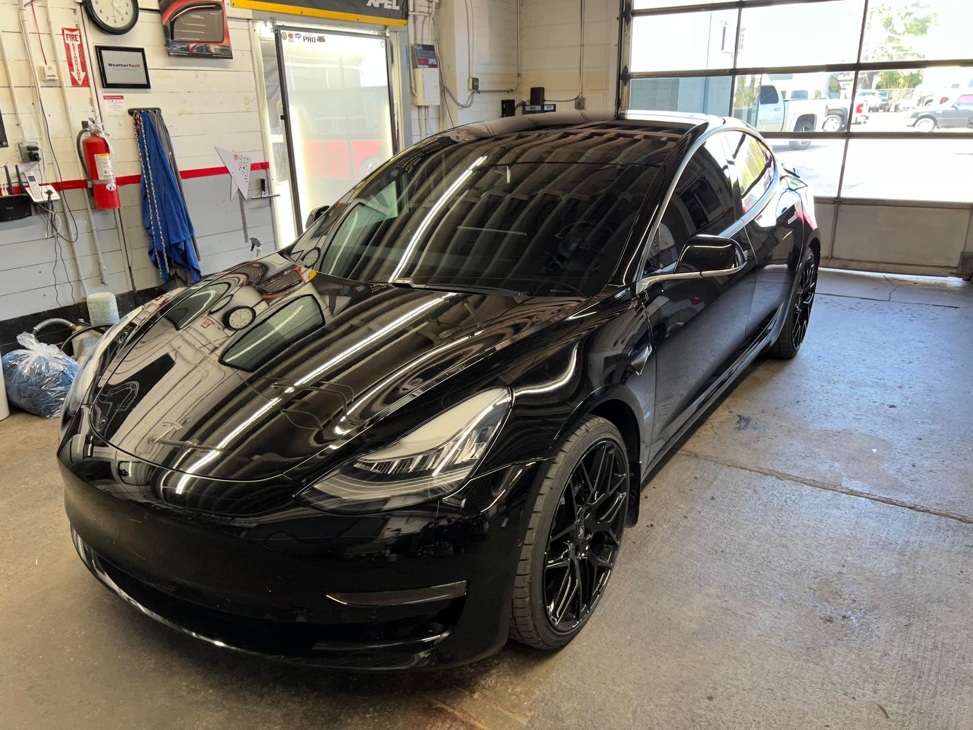 A black tesla model 3 is parked in a garage.