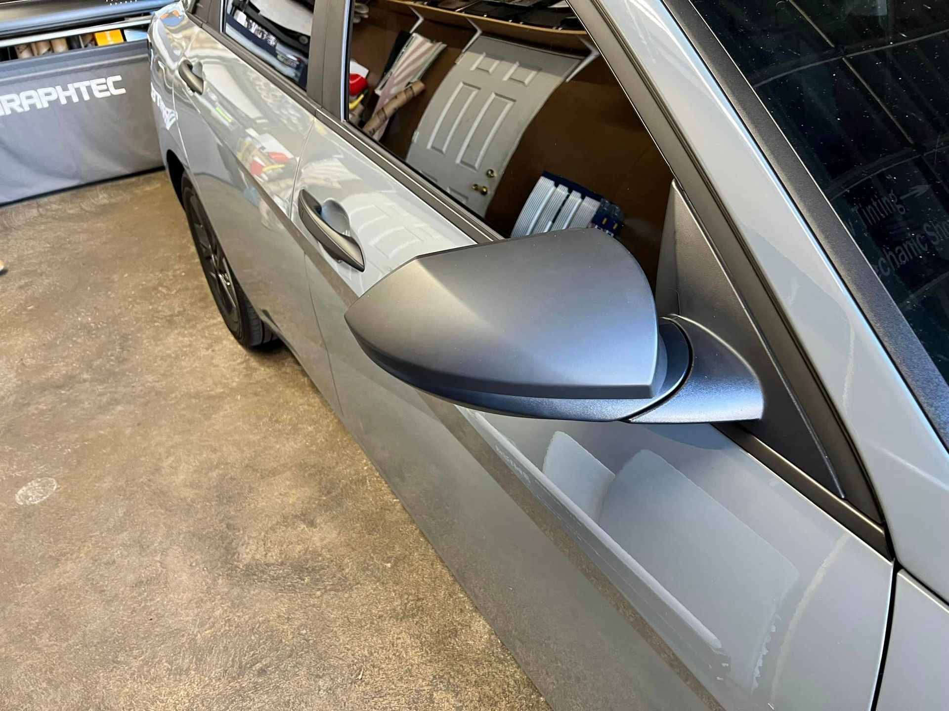 A silver car is parked in a garage with a side view mirror.