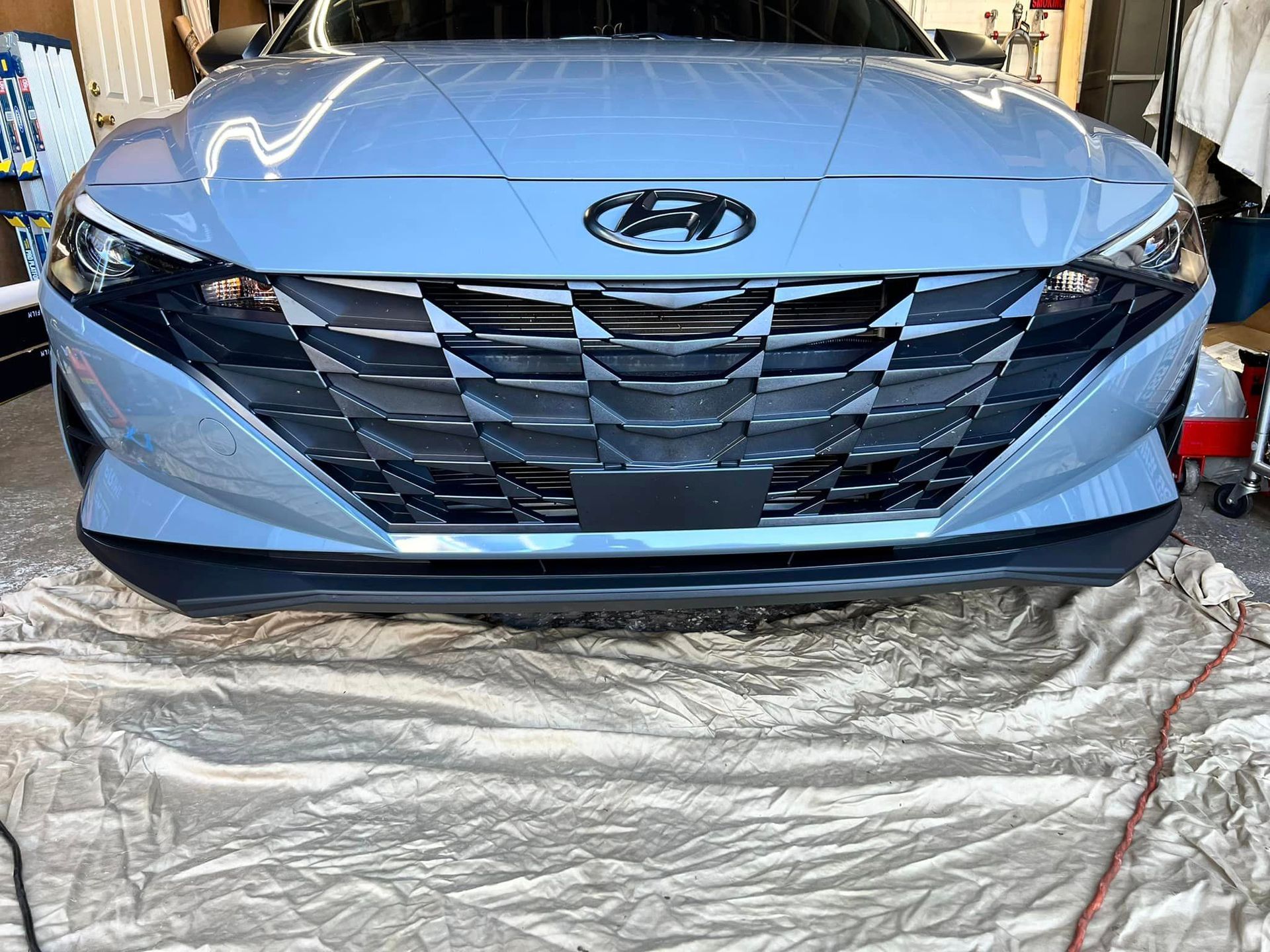 The front of a blue hyundai elantra is sitting on top of a white tarp.