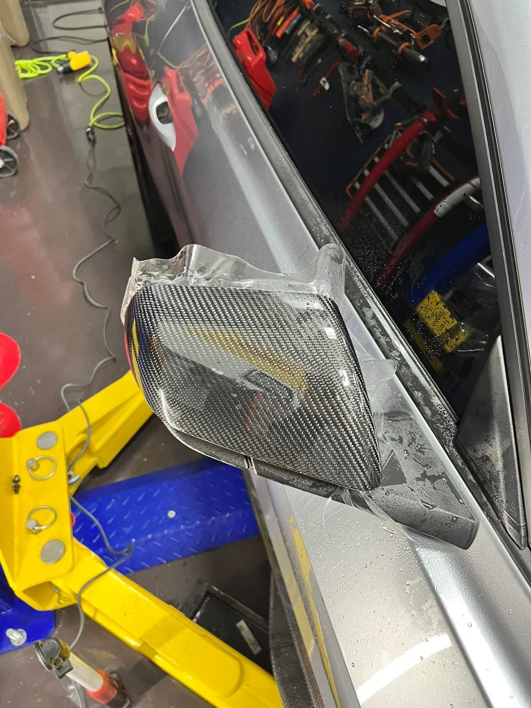 A car with a broken side mirror is on a yellow lift