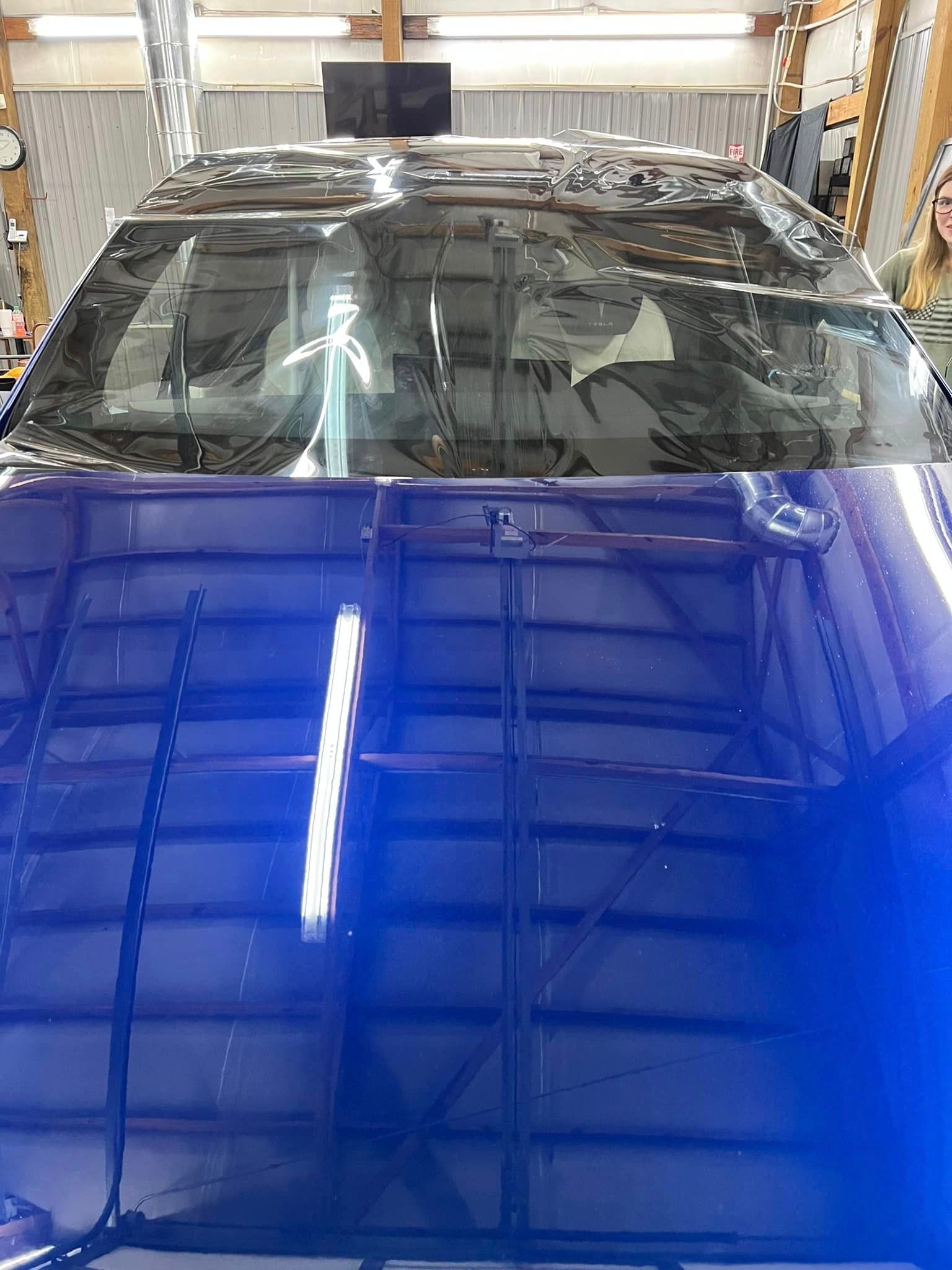 The hood of a blue car is sitting in a garage.