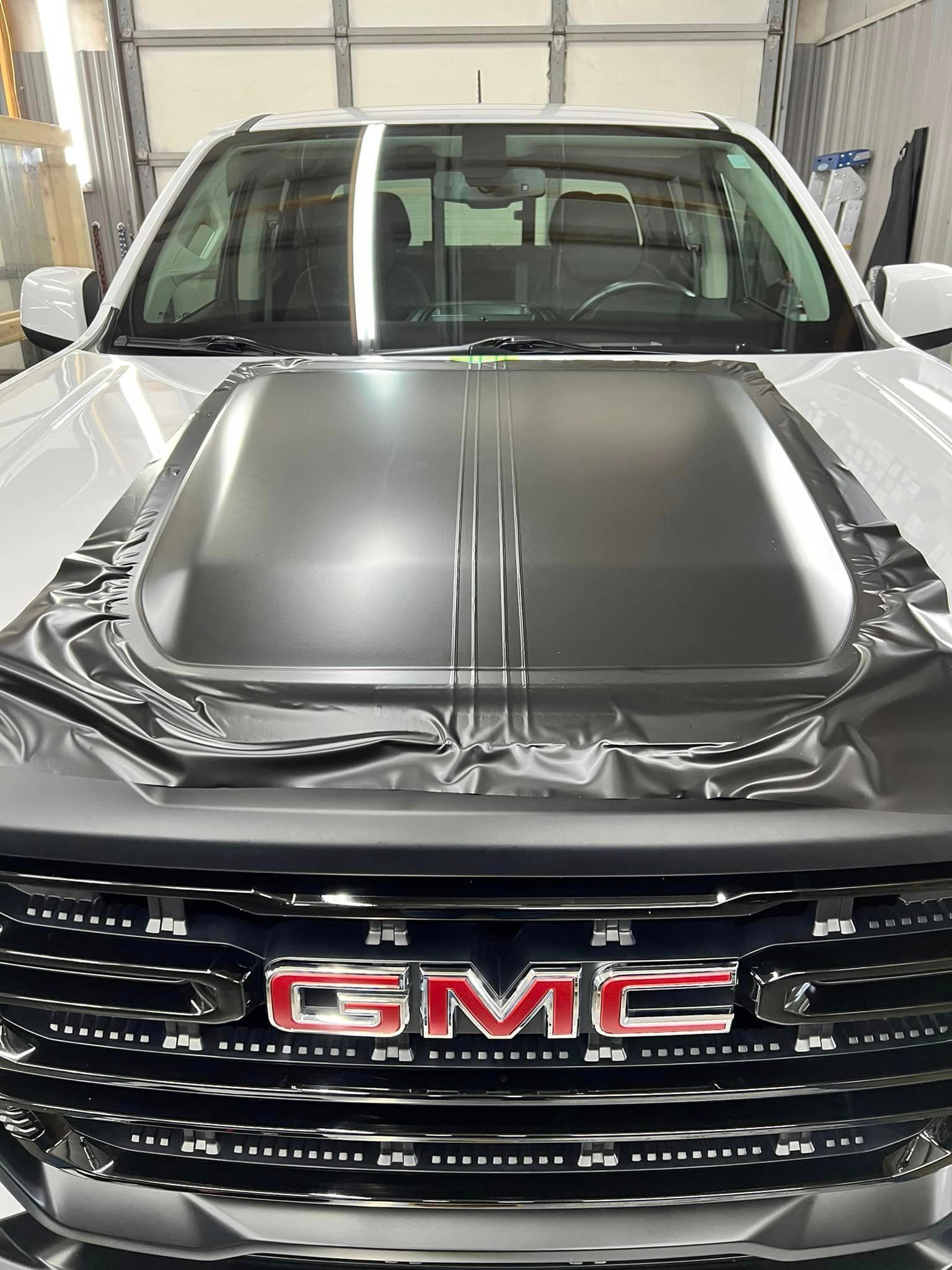 A white gmc truck with a black hood is parked in a garage.