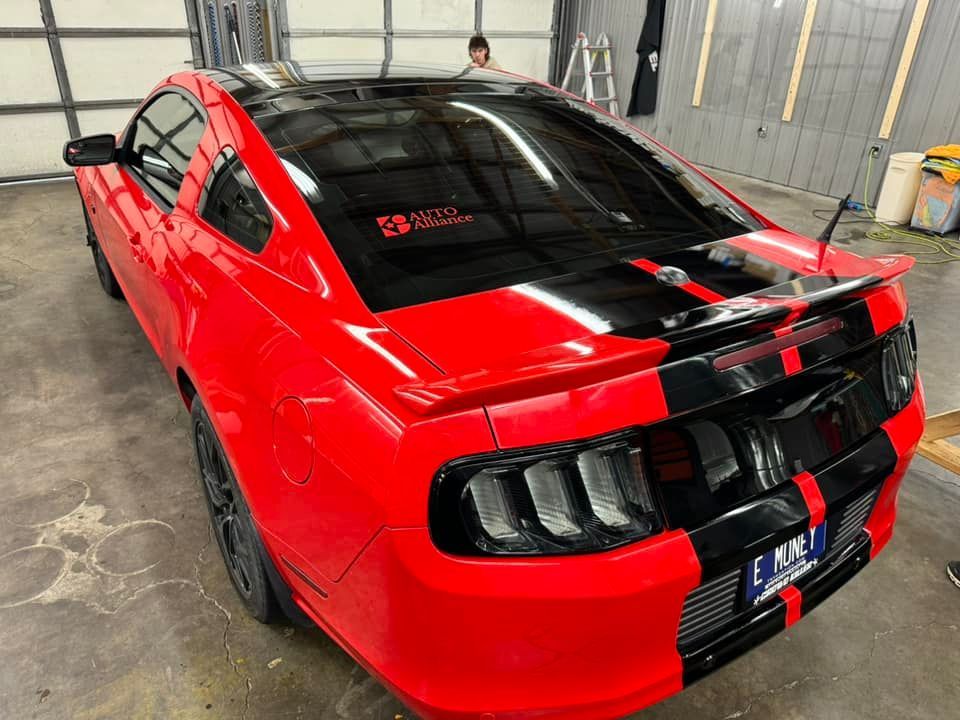 A red mustang with black stripes is parked in a garage.