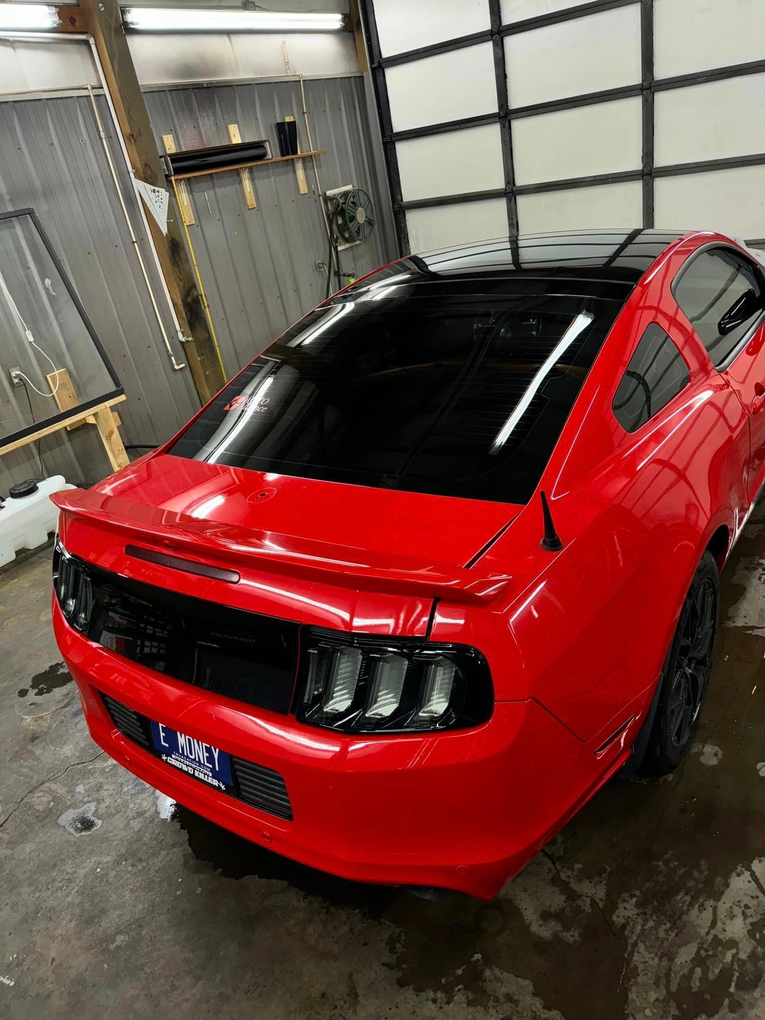 A red mustang with a black roof is parked in a garage.