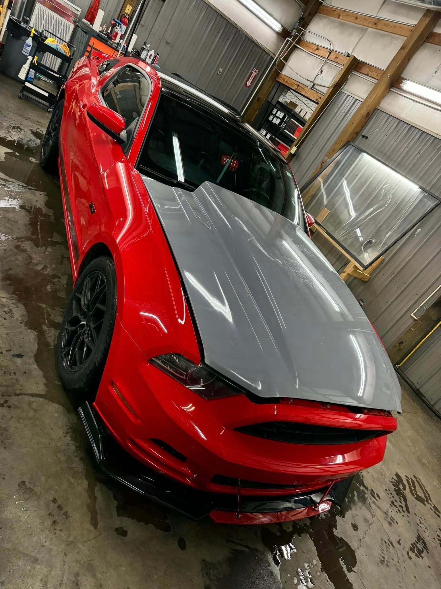A red mustang with a gray hood is parked in a garage.