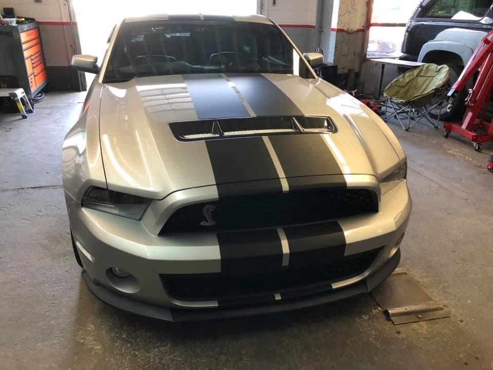 A silver mustang with black stripes on the hood is parked in a garage.