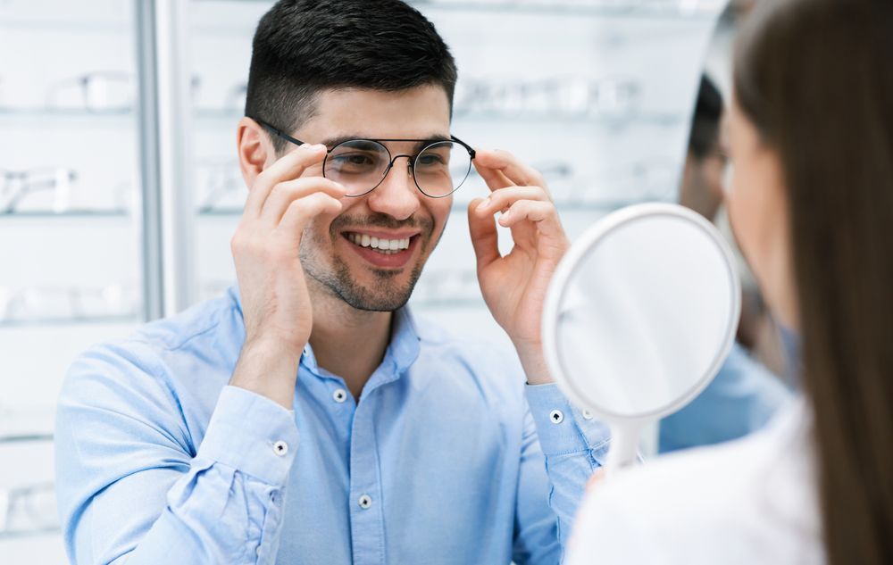 A man is trying on glasses in front of a mirror — Ian Emslie Optometrist In Warners Bay, NSW