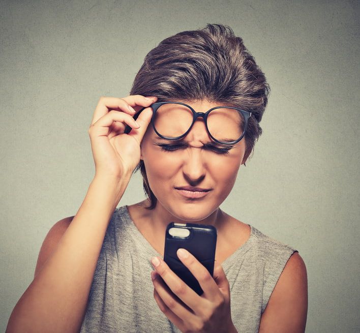 A Woman Wearing Glasses is Looking at Her Phone — Ian Emslie Optometrist In Warners Bay, NSW