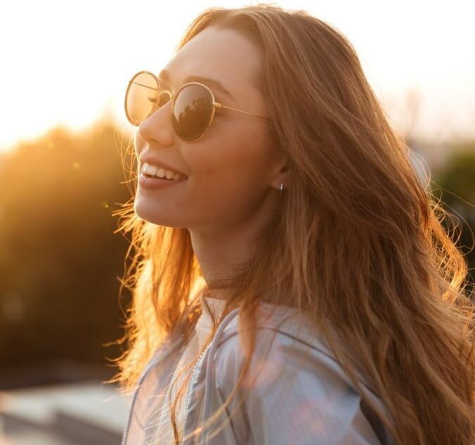 A Woman Wearing Sunglasses is Smiling and Looking to the Side — Ian Emslie Optometrist In Warners Bay, NSW