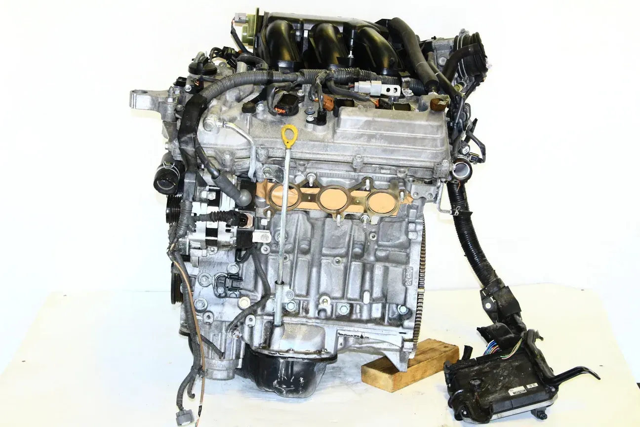 A silver, four-cylinder automotive engine with intake manifold and wiring harness on a white surface.