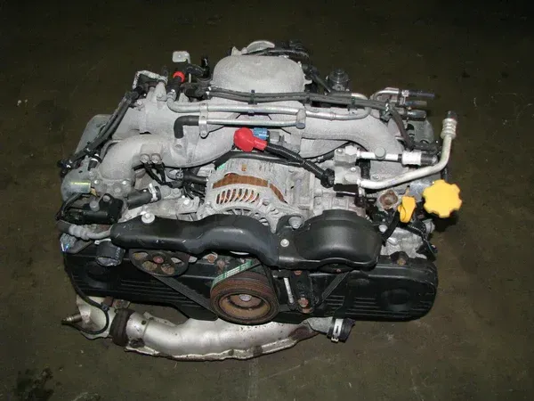 A Subaru flat-four engine shown from the front, featuring silver intake manifolds, black timing covers, and a yellow cap.